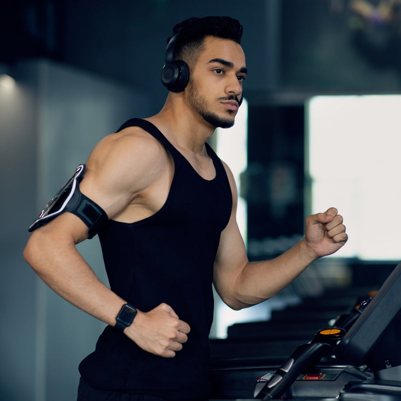 Man on a treadmill wearing headphones and a black tank top in a gym setting